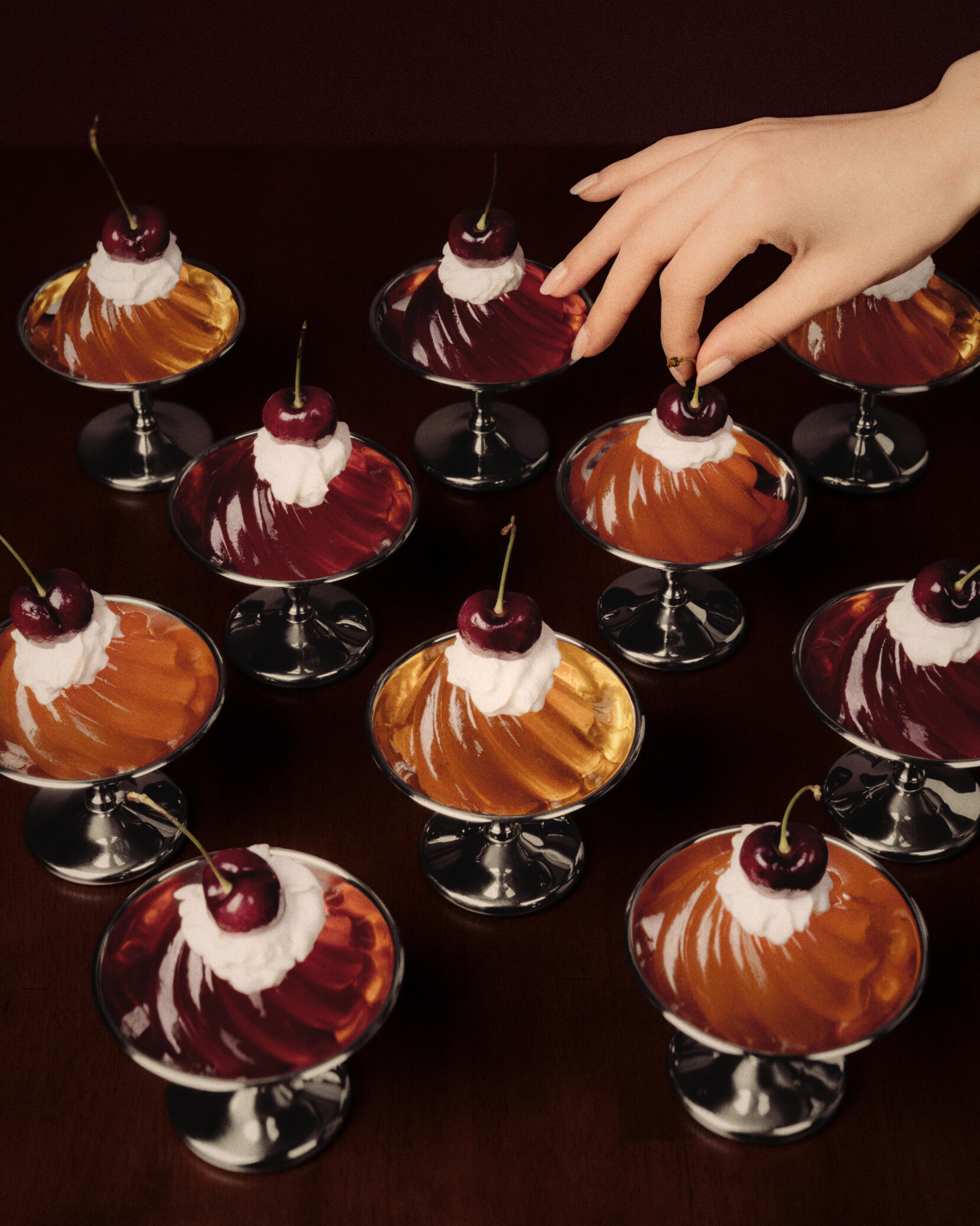 Dessert glasses with cherry-topped multi colored gelatin on a dark surface, with a hand reaching in.