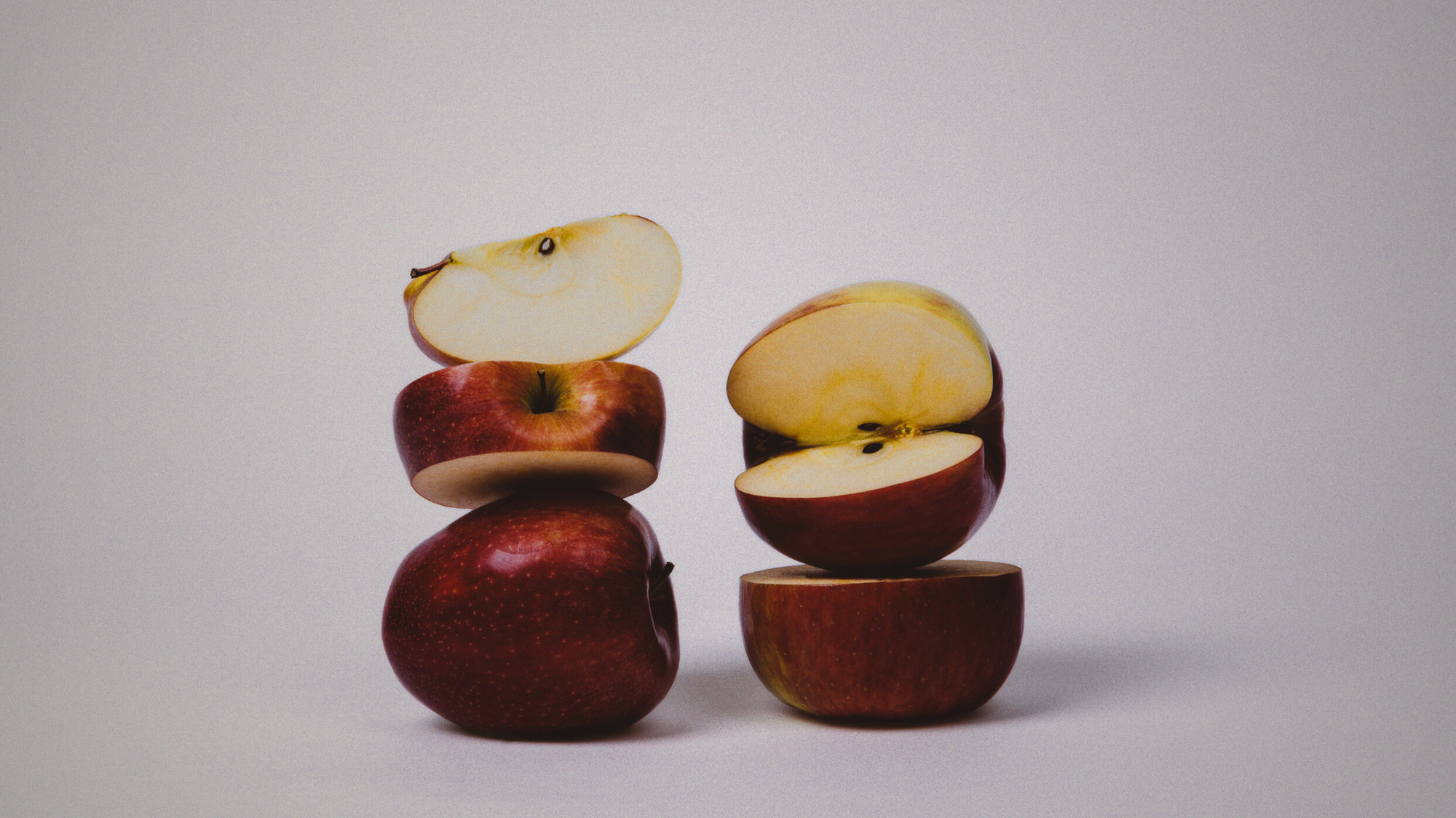 Stack of whole and halved apples on a white background