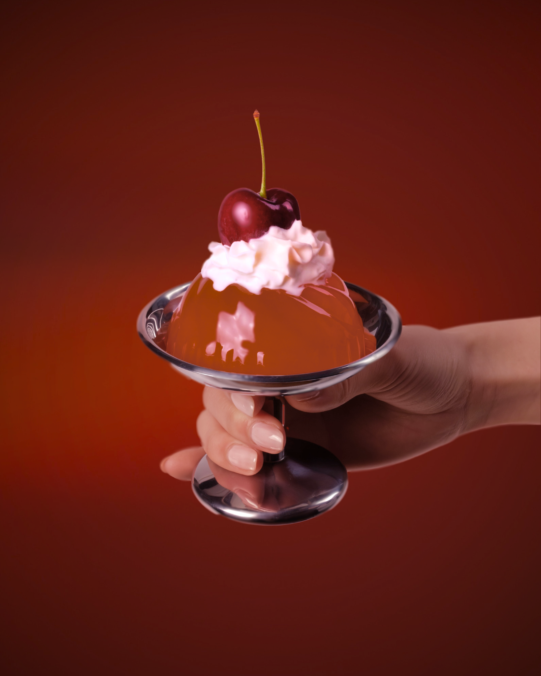 Hand holding gelatin with whipped cream, and a cherry on a red background