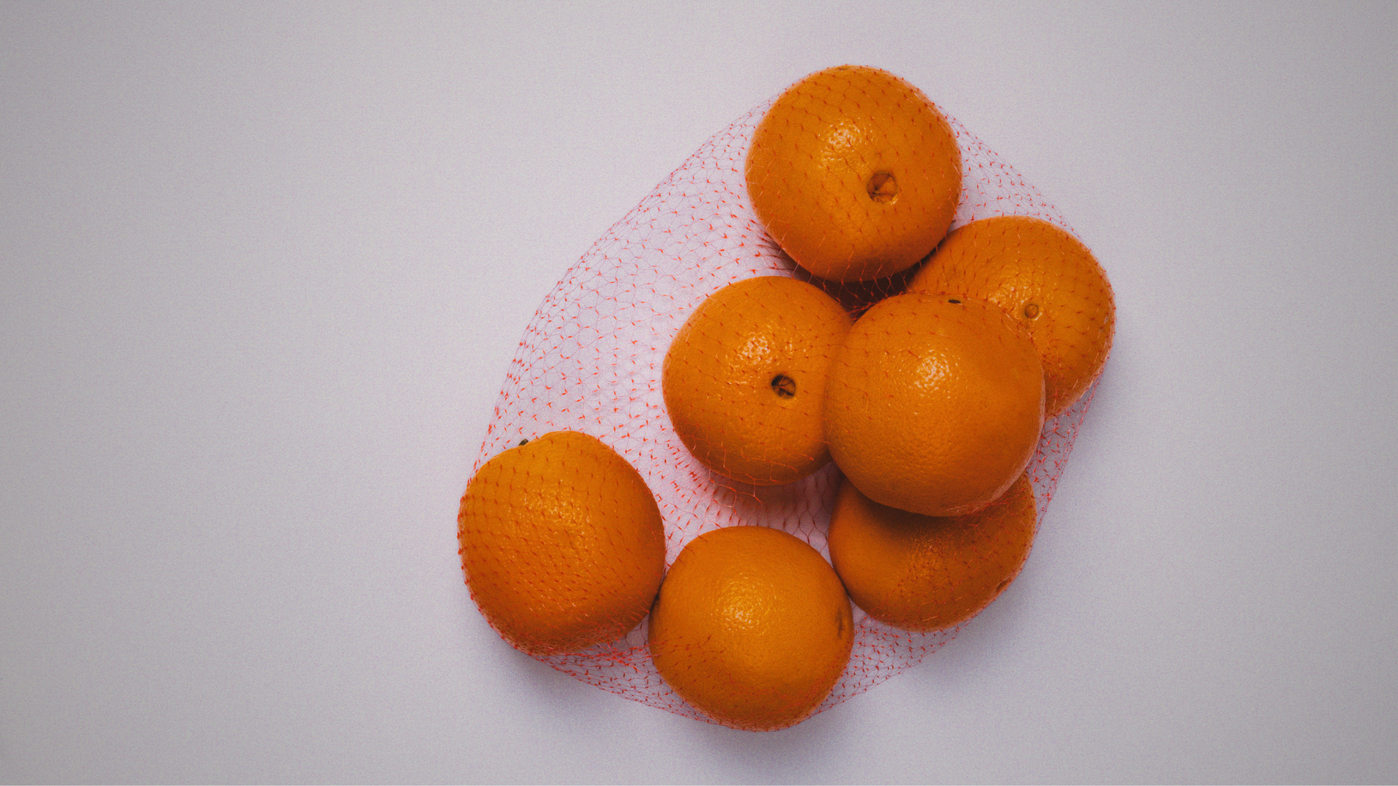 Oranges on a white background in a red net fruit bag