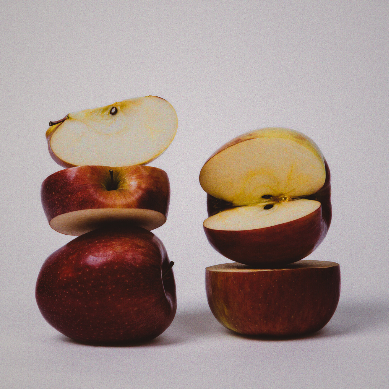 Stack of whole and halved red apples on a white background