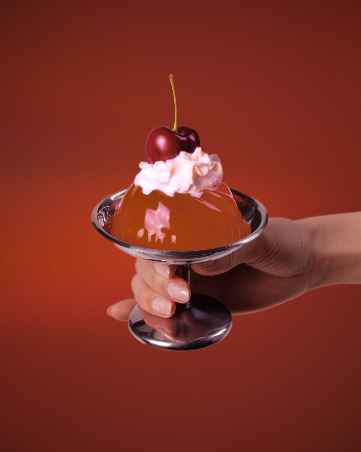 Hand holding gelatin with whipped cream, and a cherry on a red background